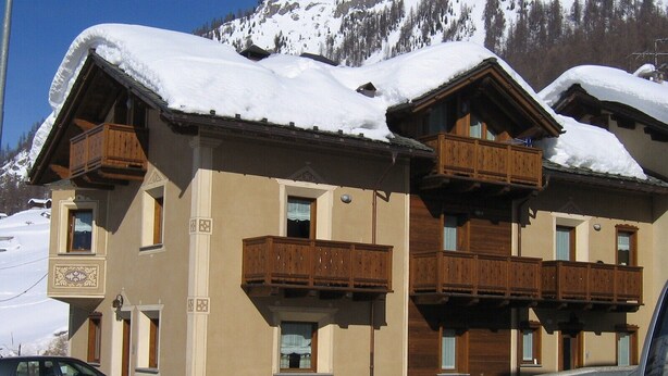 Un immeuble à plusieurs étages doté de balcons en bois, une piste de ski en arrière-plan et une voiture garée devant.