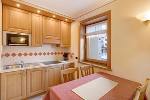 A compact kitchen with wooden cabinets, a built-in oven, a window with a view, and a dining area with a table and chairs.