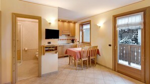Une cuisine avec une table à manger, des chaises, un téléviseur et une fenêtre donnant sur un paysage enneigé.