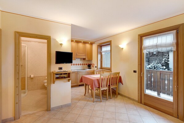 A kitchen with a dining table, chairs, a TV, and a window with a view of a snowy landscape.