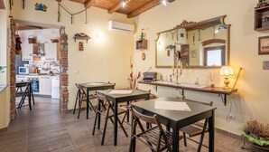A rustic interior with exposed brick walls, wooden beams, a dining area with tables and chairs, a kitchen with modern appliances, and a large mirror above the counter. - Villa "Giovanna" with Shared Open Pool, Terrace, Garden & Wi-Fi (Capannori)