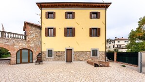 A building with a yellow facade, stone archway entrance, and a tiled courtyard. - Villa "Giovanna" with Shared Open Pool, Terrace, Garden & Wi-Fi (Capannori)
