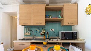Cocina compacta con armarios de madera, un microondas, un fregadero y una mesa con tazas amarillas.