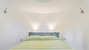 Una cama con una colcha a rayas, dos lámparas de pared y un techo curvo.
