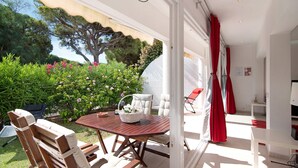 An open-plan living area with a dining table, chairs, and a view of a garden with trees and bushes. - Holiday Apartment 'Large Apartment in Vale do Lobo' with Private Garden & Wi-Fi (Almancil)