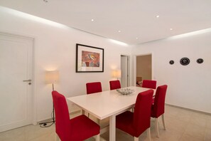 Un coin repas avec une table blanche et des chaises rouges, un tableau encadré au mur et deux lampes fixées au mur.