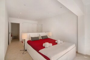 Une chambre d’hôtel avec un grand lit, des murs blancs, une couvre-lit rouge et une lampe sur pied.