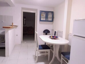 Compact kitchen area with a dining table and chairs, featuring a refrigerator and a sink.
