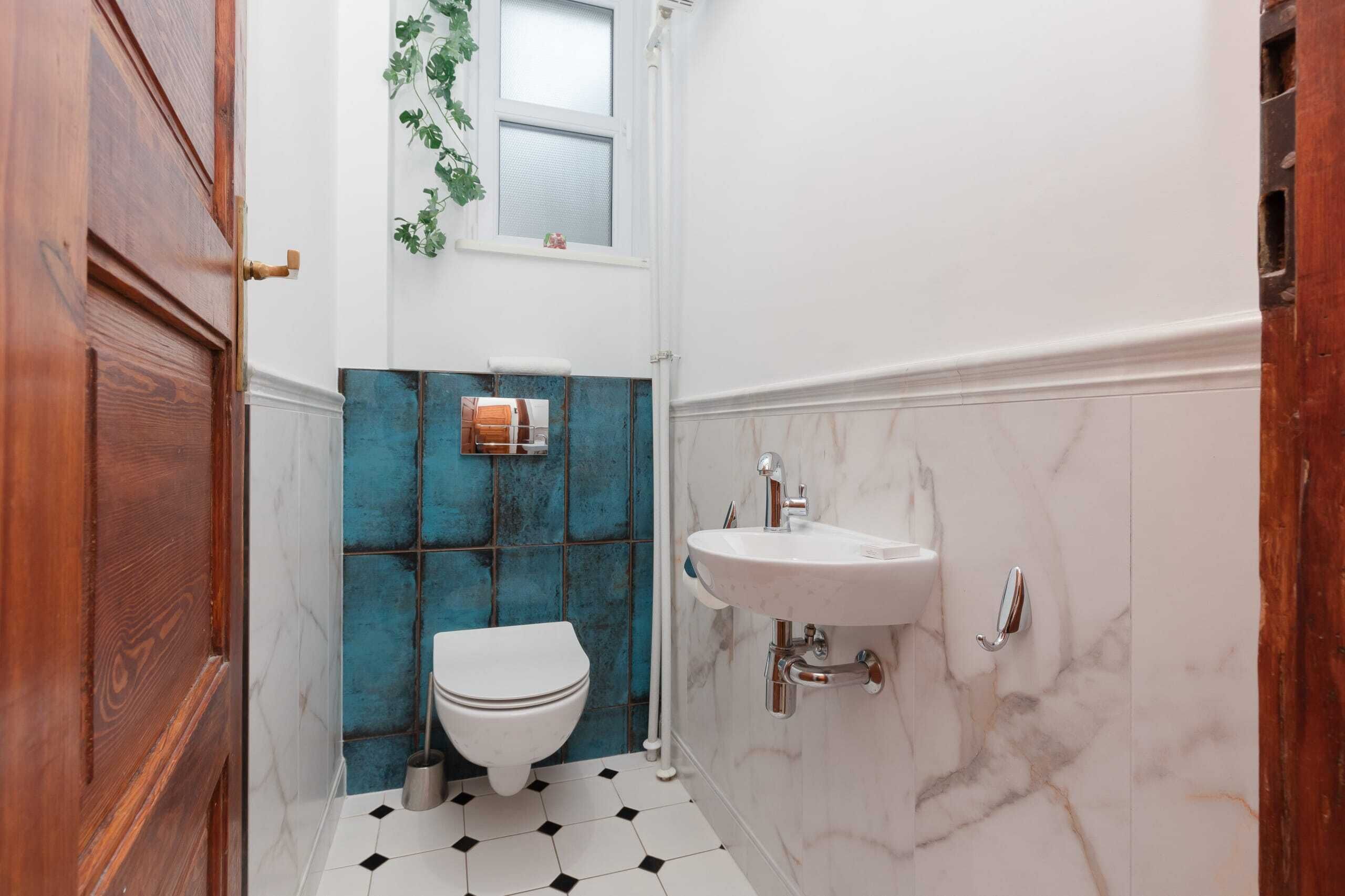 Un baño con inodoro blanco, lavamanos y ventana con planta.