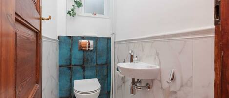Un baño con inodoro blanco, lavamanos y ventana con planta.
