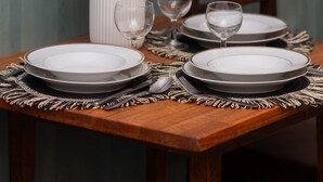 A dining table set with white plates, silverware, and a vase of white flowers.