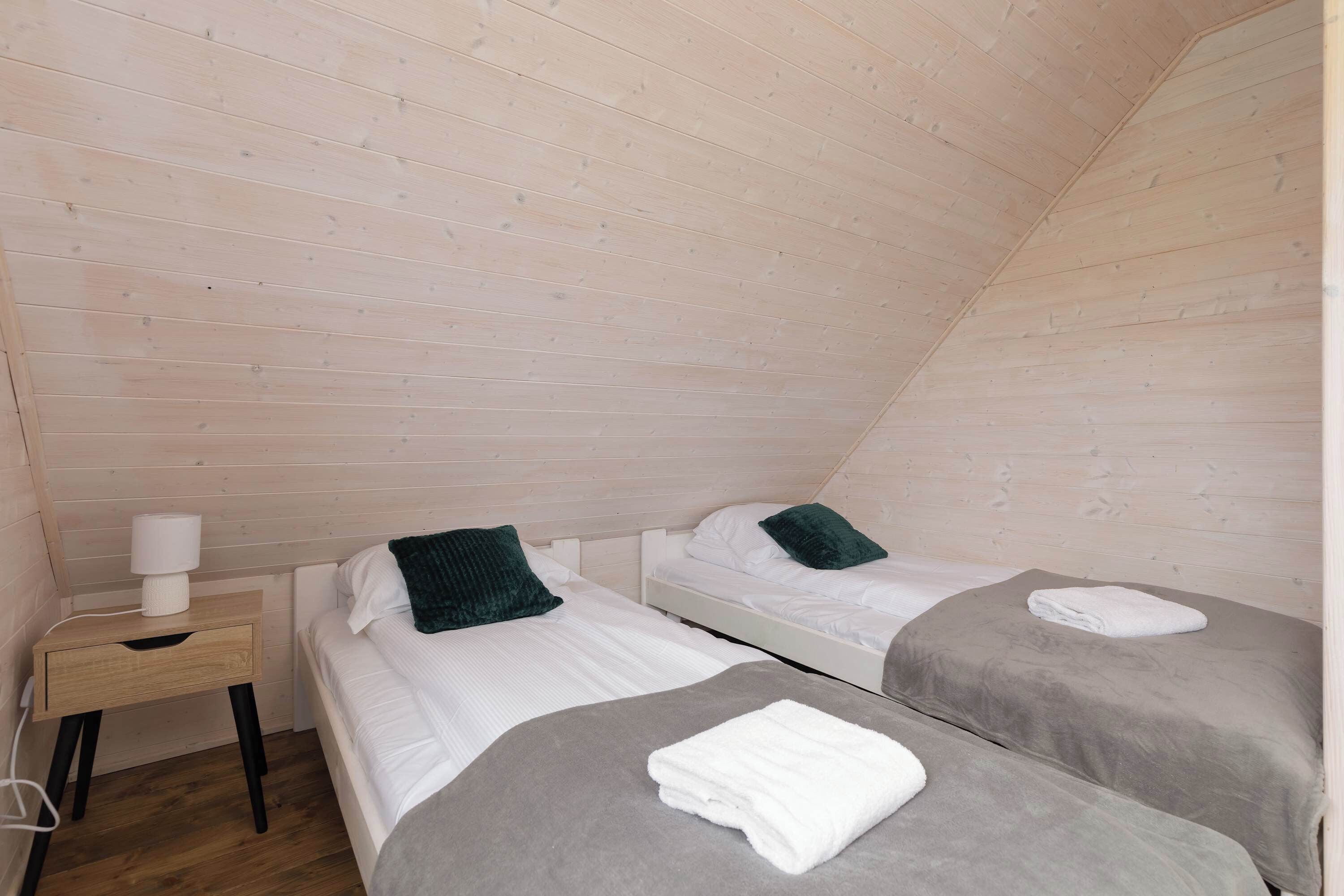 A small, cozy room with two beds, a nightstand, and a lamp.