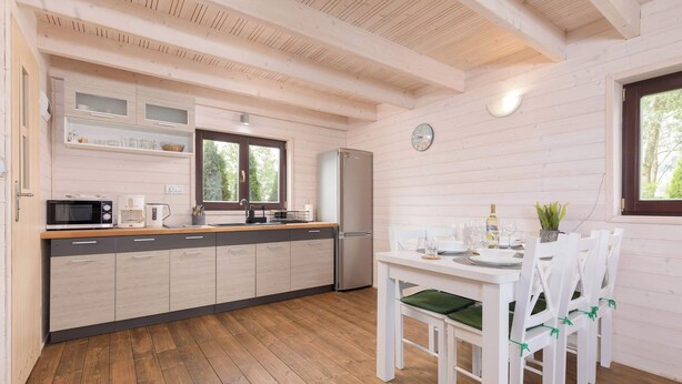 A modern kitchen with wooden cabinetry, a dining table with chairs, and a refrigerator. - Apartment with Garden | Parking, 4.9 km to the Beach (Powiat koszaliński)