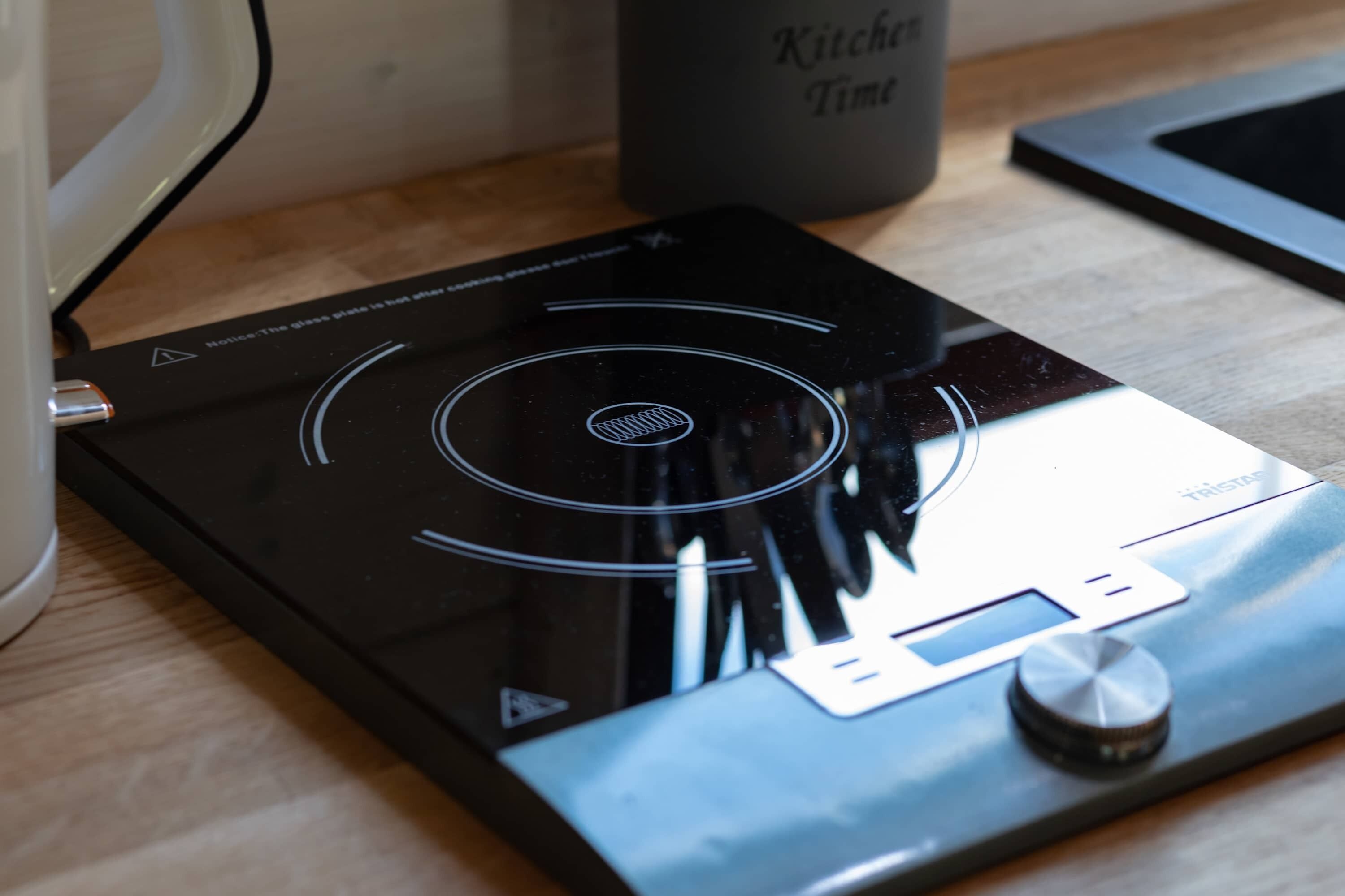 Une cuisine équipée d’une plaque de cuisson à induction noire, d’un écran numérique et d’une bouilloire.
