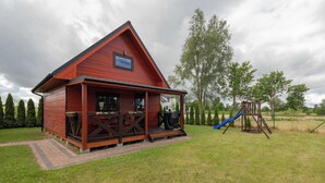 A red wooden cabin with a porch, a blue slide, and a wooded area in the background. - Apartment with Garden | Parking, 4.9 km to the Beach (Powiat koszaliński)