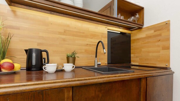 A kitchen with a wooden countertop, a black kettle, a white cup, a small potted plant, and a sink.