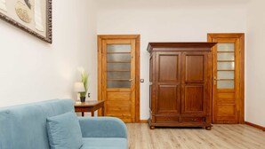 A room with a blue sofa, wooden wardrobe, and a small table with a lamp.