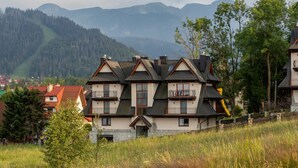 A multi-story chalet with a sloped roof, balconies, and a stone foundation. - Atmospheric Apartment | Mountain View and Workspace (Zakopane)