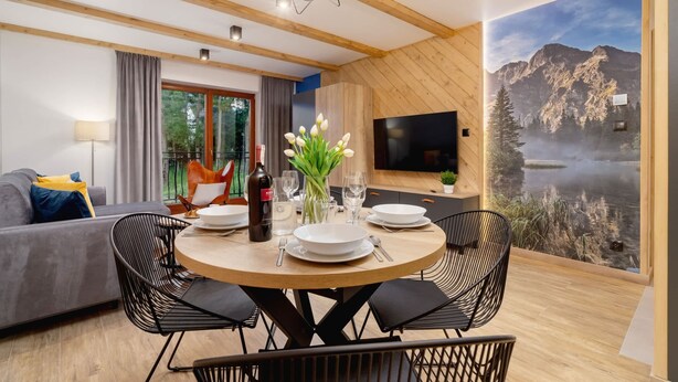 A modern dining area with a round table, black chairs, and a scenic mural of a mountain and lake. - Atmospheric Apartment | Mountain View and Workspace (Zakopane)