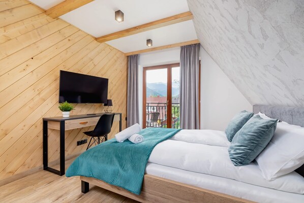 A bedroom with a bed, a desk with a chair, a TV, and a view of the outdoors.