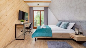 Un dormitorio moderno con techo de madera, cama con manta color turquesa, escritorio con televisor y vistas al balcón.
