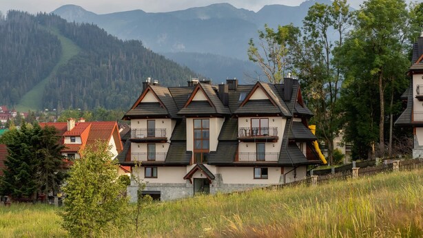Una chalet de varios pisos con tejado inclinado, balcones y base de piedra.