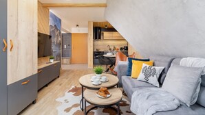 Un salón moderno con un sofá gris, una mesa de centro de madera con croissants y un televisor sobre un mueble de madera.