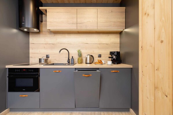 A modern kitchen with grey cabinets, a stainless steel range hood, a wooden countertop, and a built-in oven.