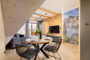 A dining area with a round table, black wire chairs, and a view of a mountainous landscape through a large window.