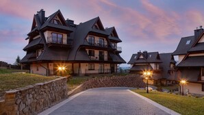 A large, multi-story house with a stone retaining wall and a paved driveway. - Stylish Apartment | Mountain View, Workspace (Zakopane)