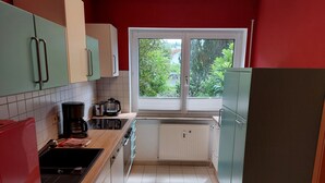 Eine kleine Küche mit weiß gefliestem Boden, einem Fenster mit Blick auf Grünflächen und einfachen Geräten.