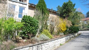 Ein Wohngebäude mit einer Steinmauer, einem Balkon und verschiedenen Sträuchern und Bäumen.