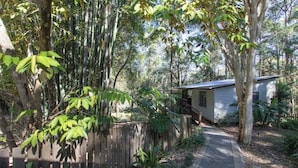 Une clôture en bois, un chemin pavé et un petit bâtiment doté d’un toit en pente, le tout situé dans une zone boisée.