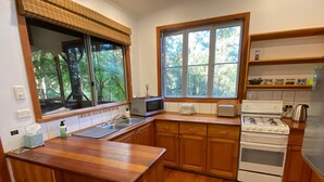 Une cuisine avec des meubles en bois, un évier en acier inoxydable, un four à micro-ondes, une cuisinière et une fenêtre donnant sur les arbres.