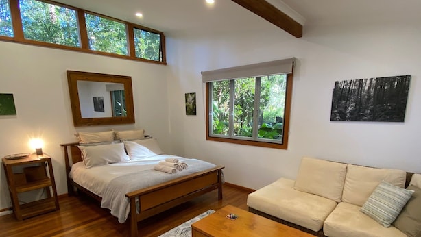Une chambre à coucher avec un lit en bois, une table de chevet, un canapé et une fenêtre donnant sur des arbres.