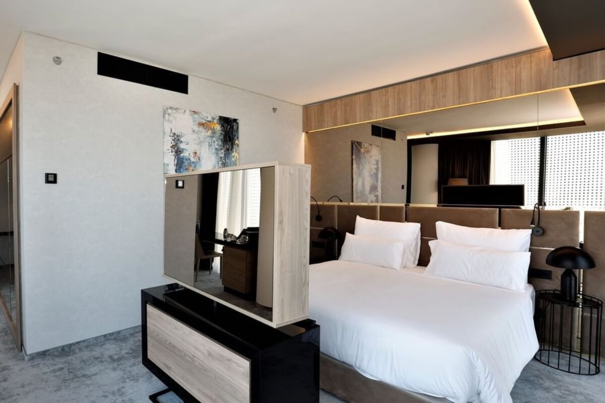 A modern hotel room with a large bed, a desk with a chair, a television, and a large mirror.