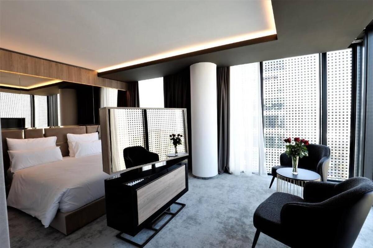 A modern hotel room with a bed, a TV, a desk, and a chair.