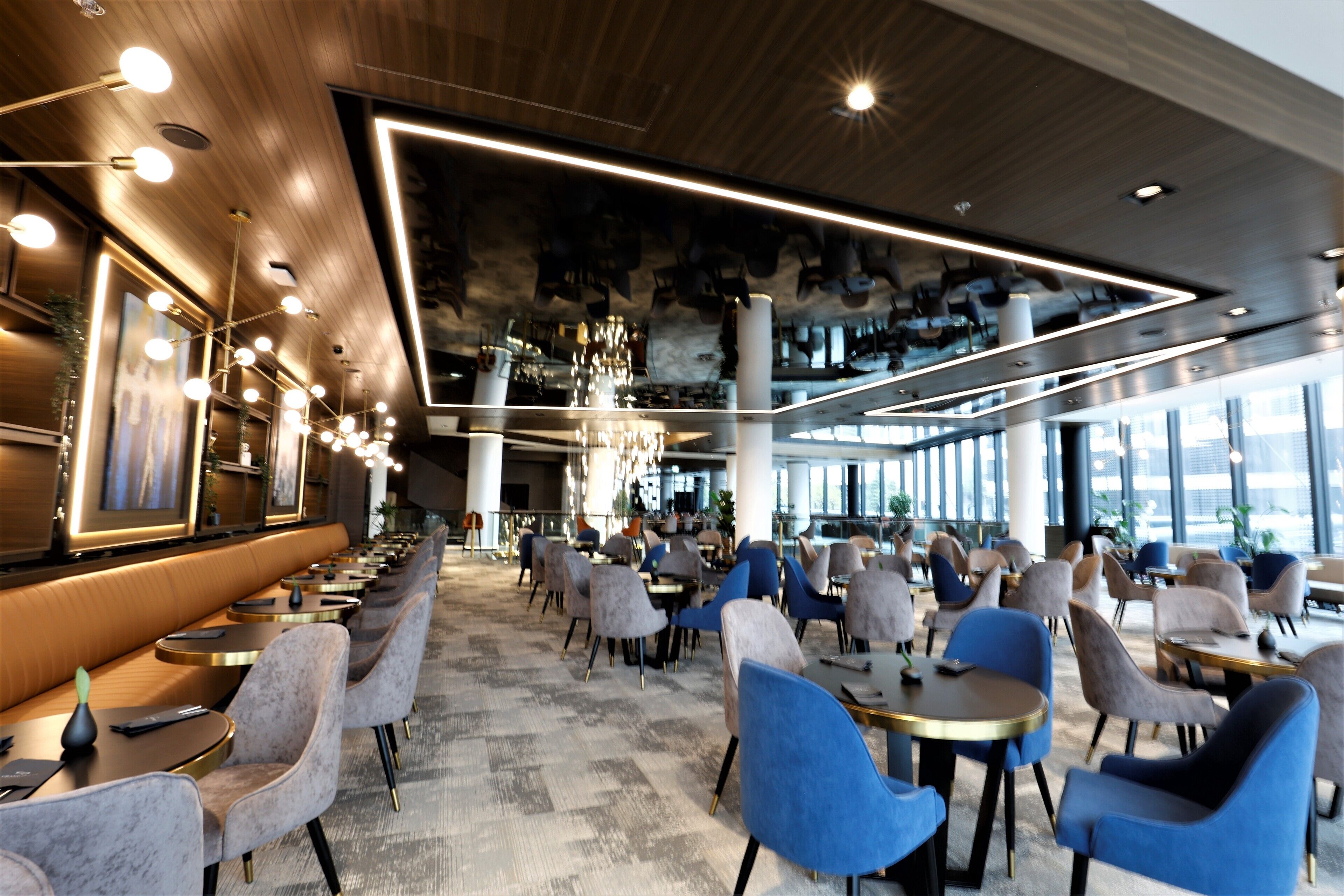 A modern restaurant with a long counter, multiple tables, and chairs.