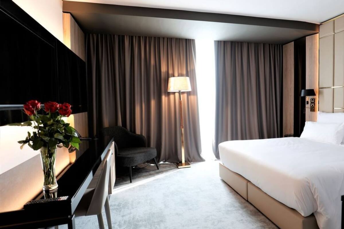 A hotel room with a bed, a desk with a lamp, a chair, and a vase of flowers.