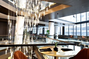 A modern interior with a glass railing, a round table with a vase, and hanging lights. - Grand Plaza Hotel and Congress Centre (Ljubljana)
