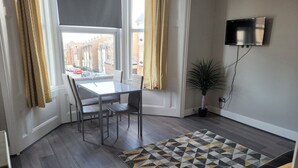 A modern living room with a glass dining table, leather sofa, and a patterned rug.