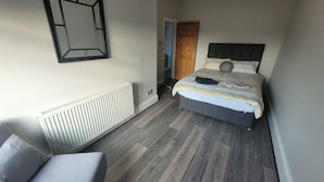 A bedroom with a bed, a radiator, a door, and a chair.