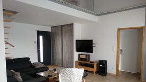 Uma sala de estar moderna com sofá, mesa de centro e televisão sobre um suporte de madeira.