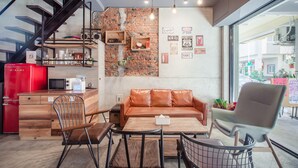 Una cocina moderna con un refrigerador rojo, un microondas y un armario de madera. Hay un sofá de cuero marrón y una mesa de comedor con sillas. Se ve una pared de ladrillo con estantes y una escalera.