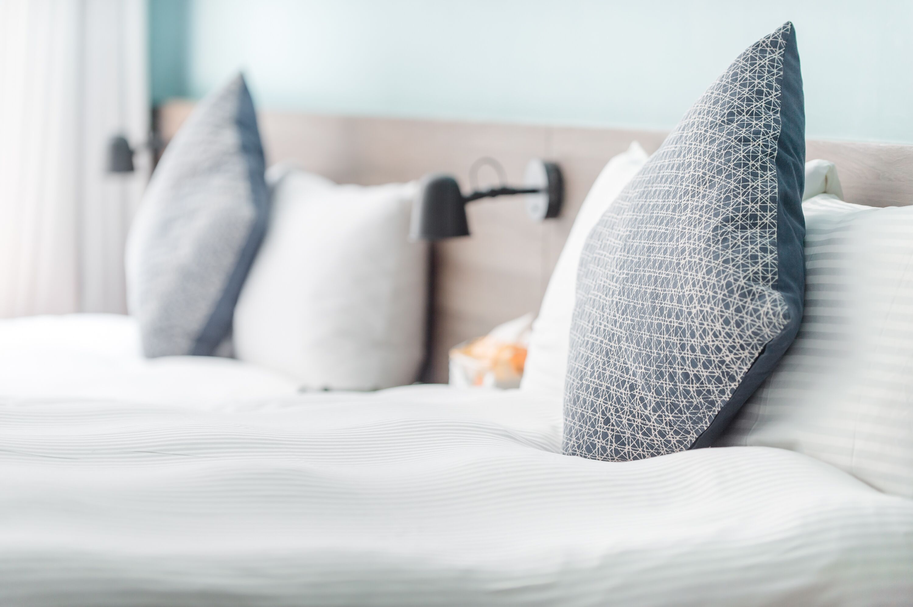 Una cama con ropa de cama blanca y almohadas estampadas con motivos geométricos.