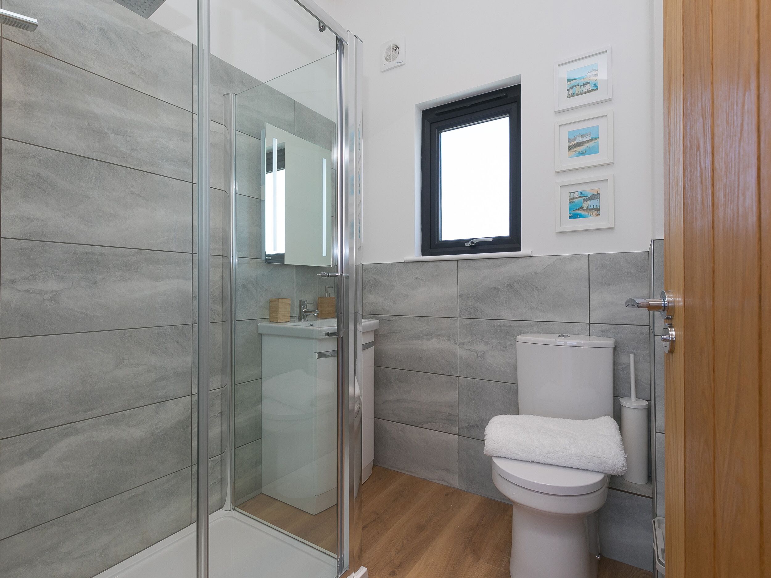 Un baño moderno con cabina de ducha de vidrio, inodoro blanco y una pequeña ventana sobre el lavamanos.