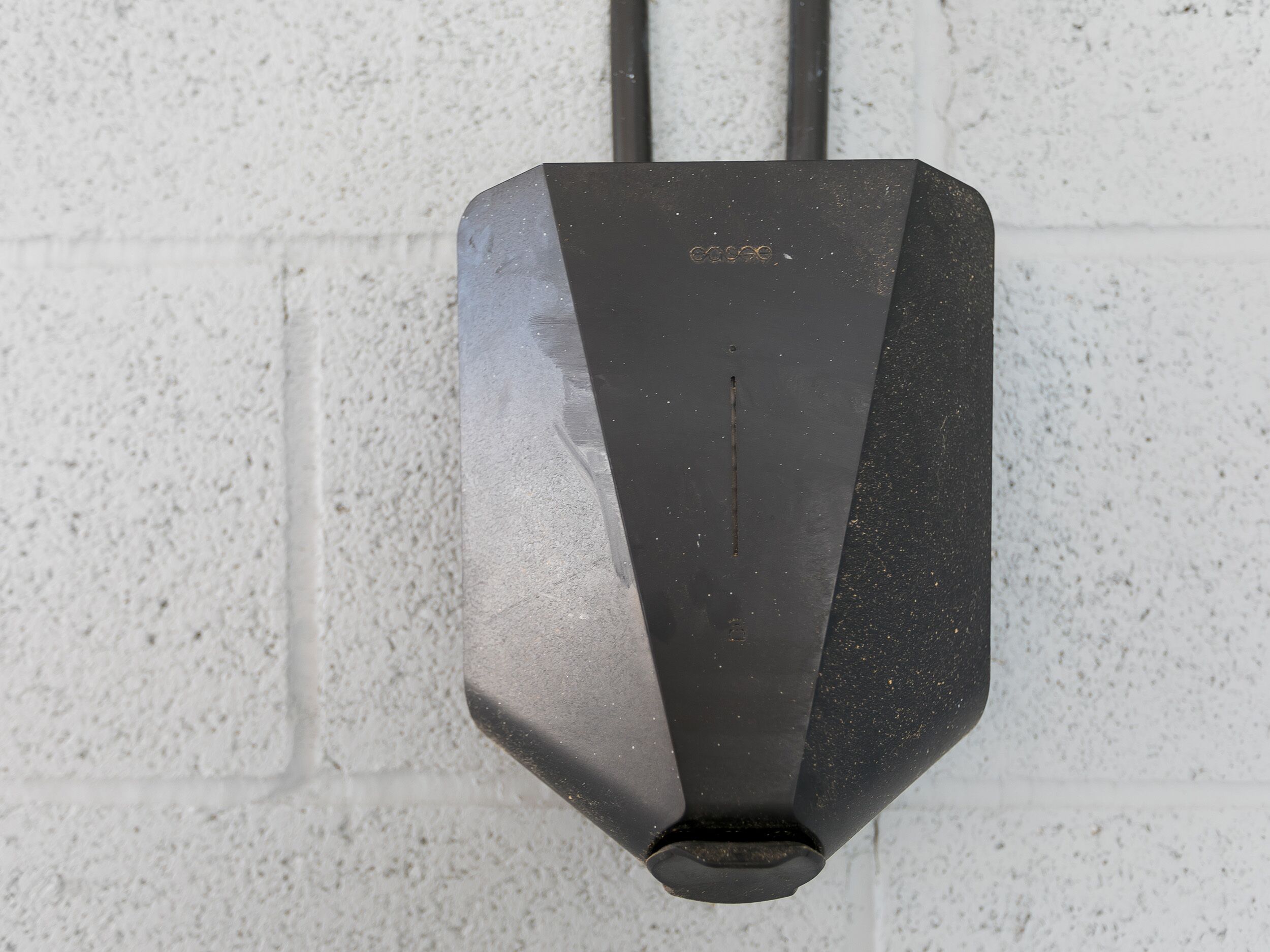 A black, rectangular object with a protruding cable, mounted on a textured white wall.
