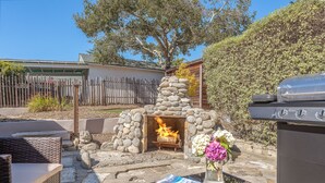 Une terrasse extérieure avec un foyer en pierre, des meubles en osier et un barbecue.