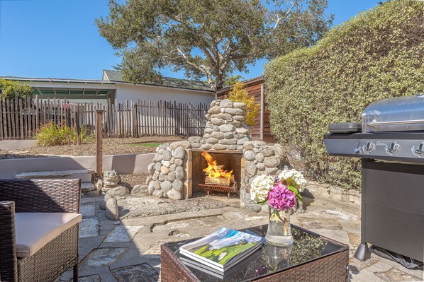 An outdoor patio with a stone fire pit, wicker furniture, and a grill.