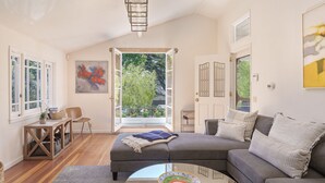 Un salon moderne avec un canapé d’angle, une table basse et une vue sur la verdure grâce à une porte ouverte.